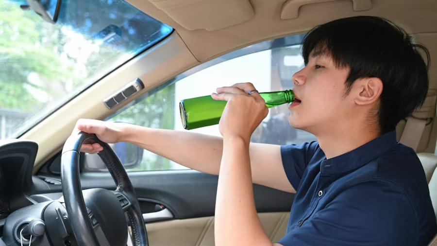A young man drinking beer while driving a car.
