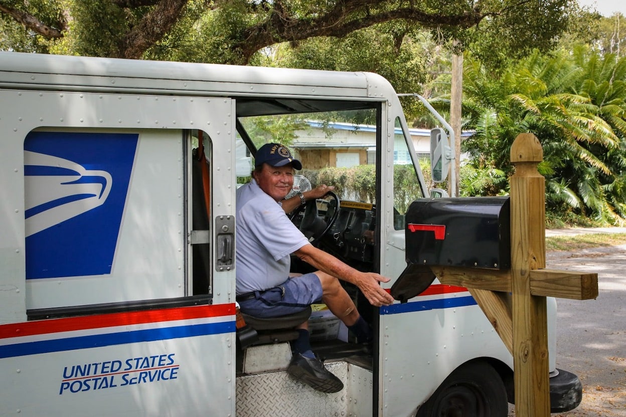 A bus driver in a blue shirt sitting on a white and blue bus during the daytime
