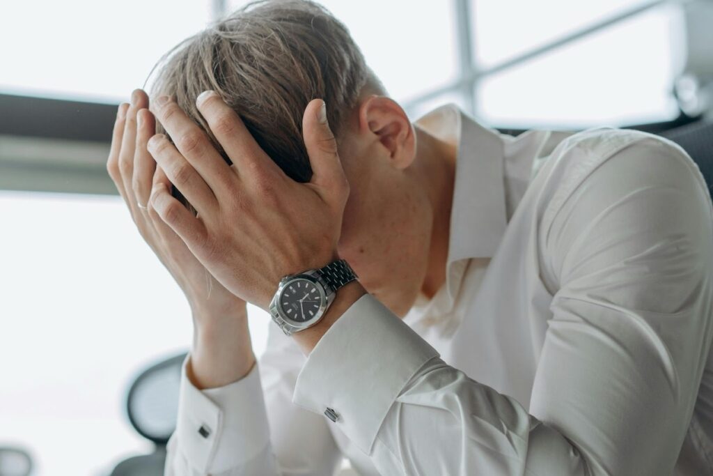 A man in a white dress shirt holding his head in his hands, visibly stressed