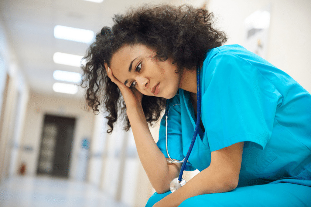 A nurse sitting in a hospital hallway, looking concerned