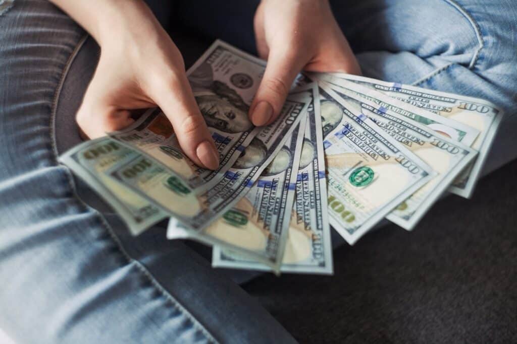 A person holding a fan of 100 U.S. dollar banknotes