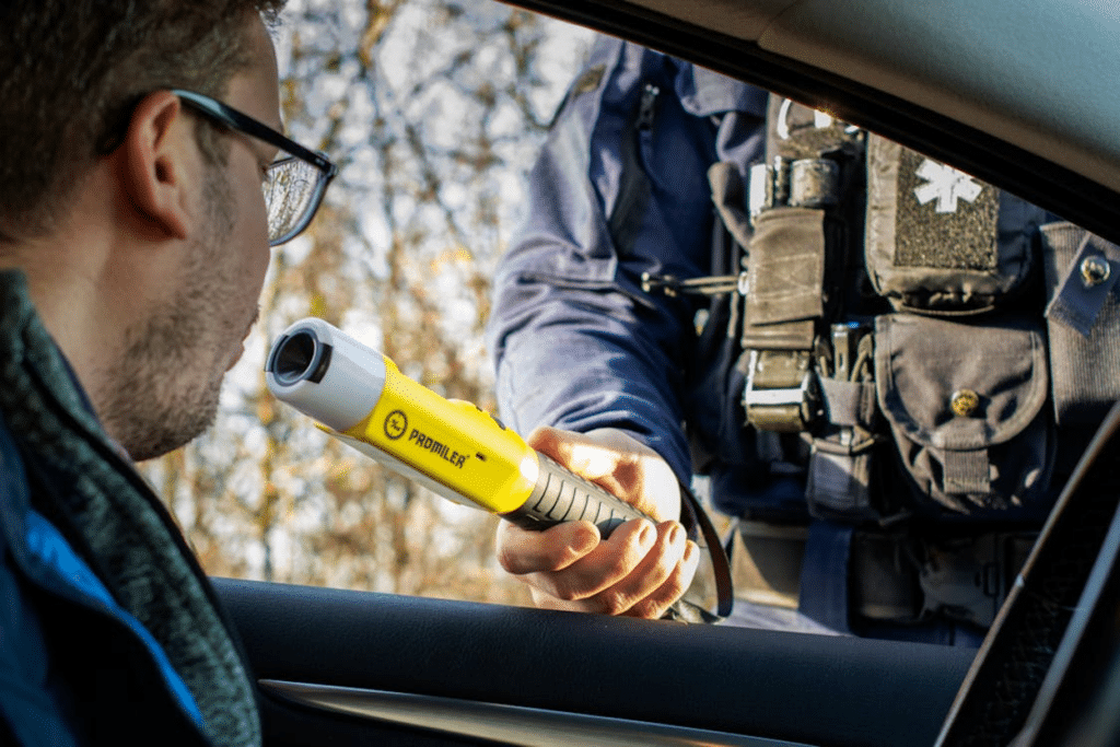 Officer holding a handheld breathalyzer device outside a driver's car window
