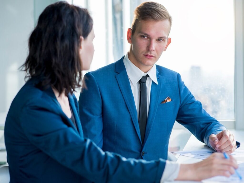 Two professionals in blue suits are having a discussion at a desk