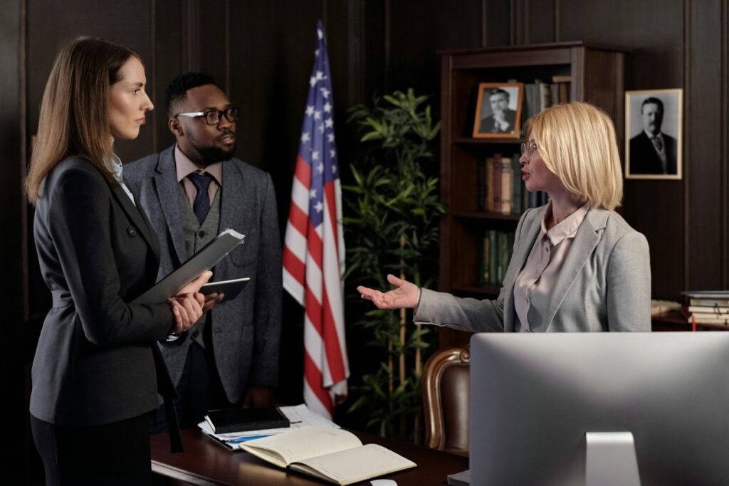 A blonde attorney speaks with two colleagues in a formal government office.