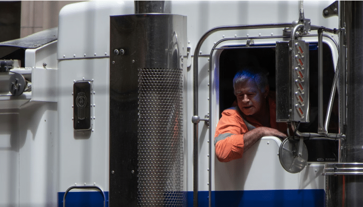 A commercial truck driver leaning out of his vehicle window, talking to someone below