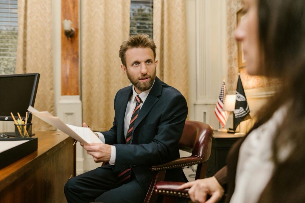 A defense attorney in a dark suit holding documents while speaking with a client