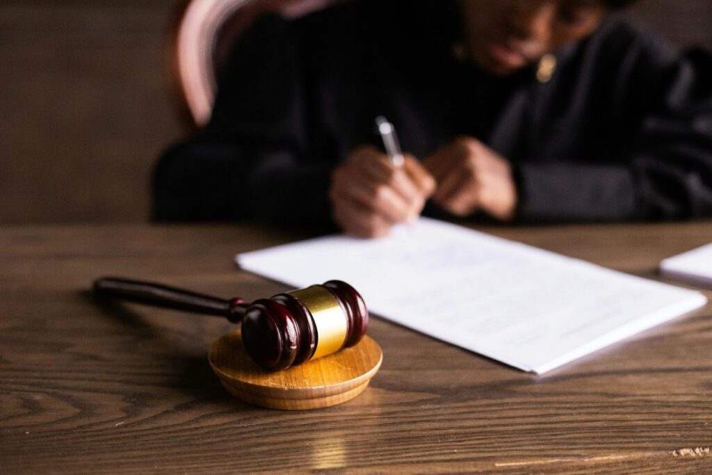 A judge in black robes writing on legal documents with a wooden gavel resting on the bench.