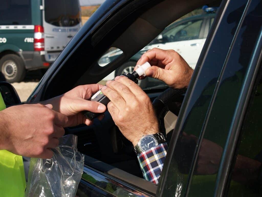 A law enforcement officer in a high-visibility vest administering a breathalyzer test
