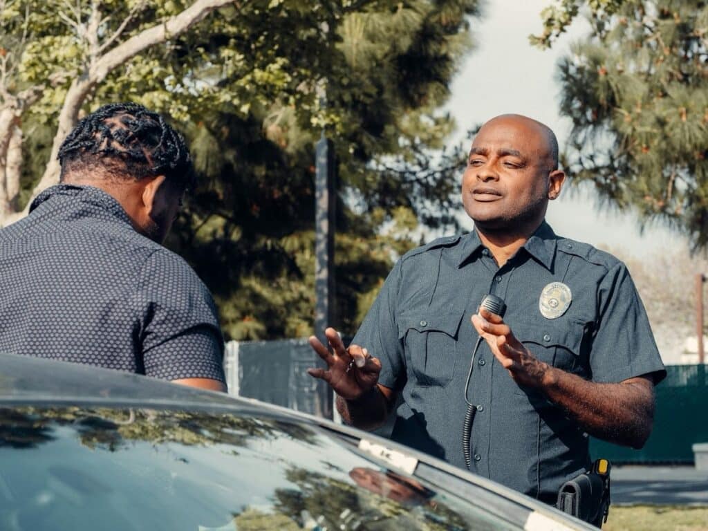 A male police officer gestures while speaking with a civilian outside of his car, indicatingcating possible DWI