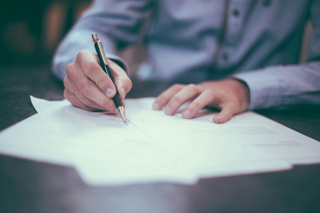 A person in a dress shirt signs legal documents at a desk