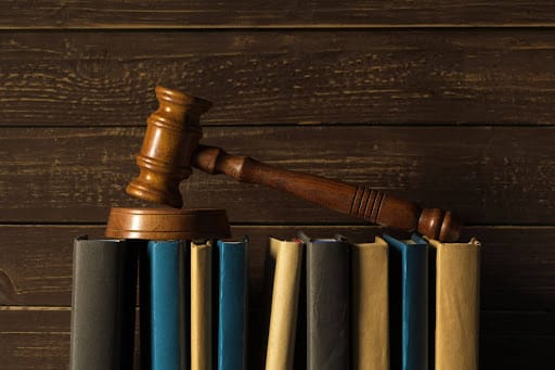 A wooden judge's gavel resting on a row of law books against a dark wooden background.