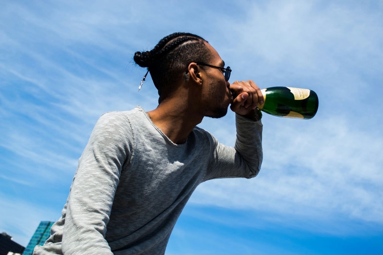 A young man drinks directly from a champagne bottle outdoors