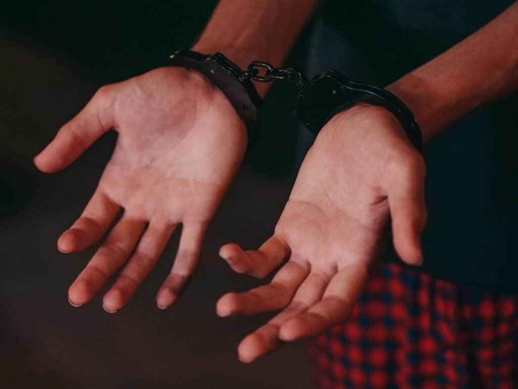 Close-up of a person's hands restrained in black handcuffs.