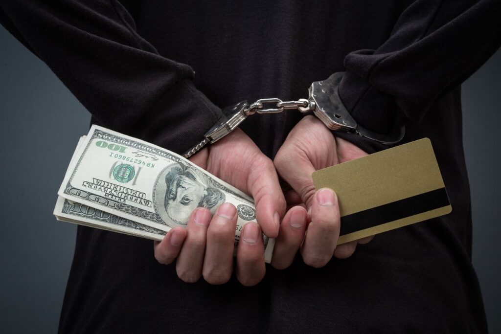 Person in handcuffs holding dollar bills and a credit card behind their back