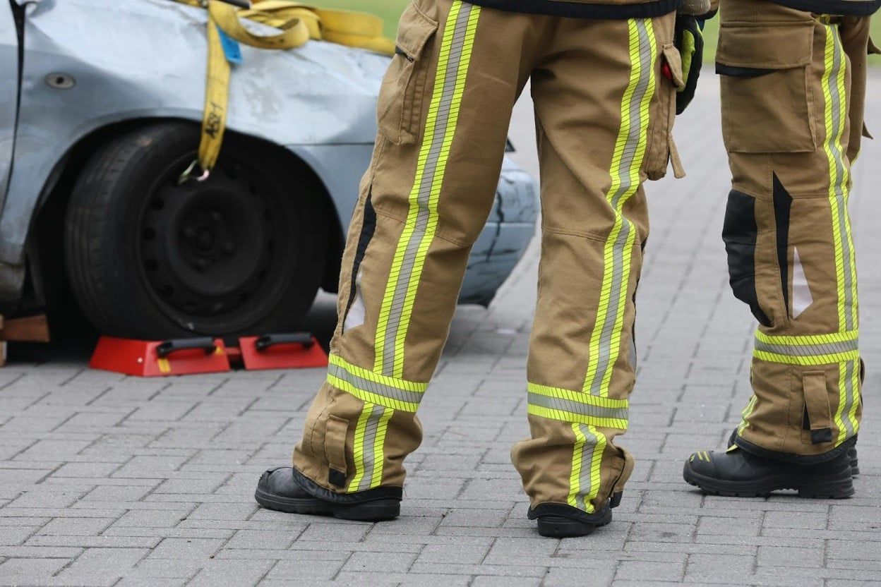 Two firefighters in high-visibility gear standing beside a heavily damaged car