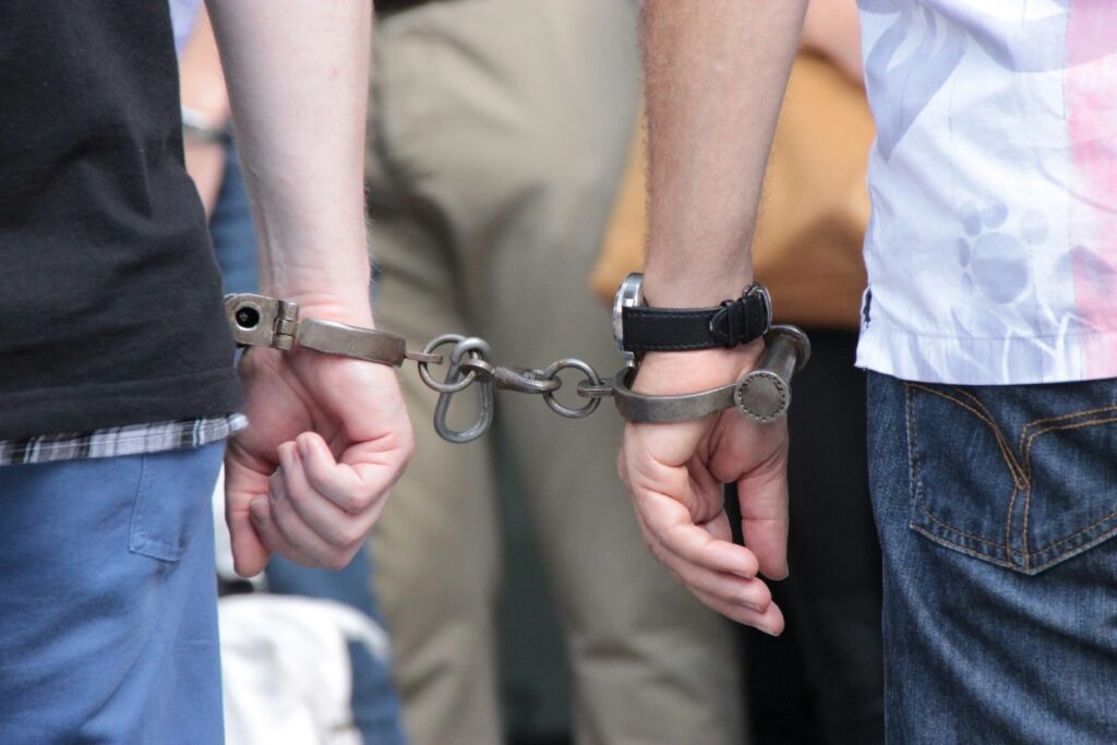 Two individuals standing side by side, their wrists bound with metal handcuffs